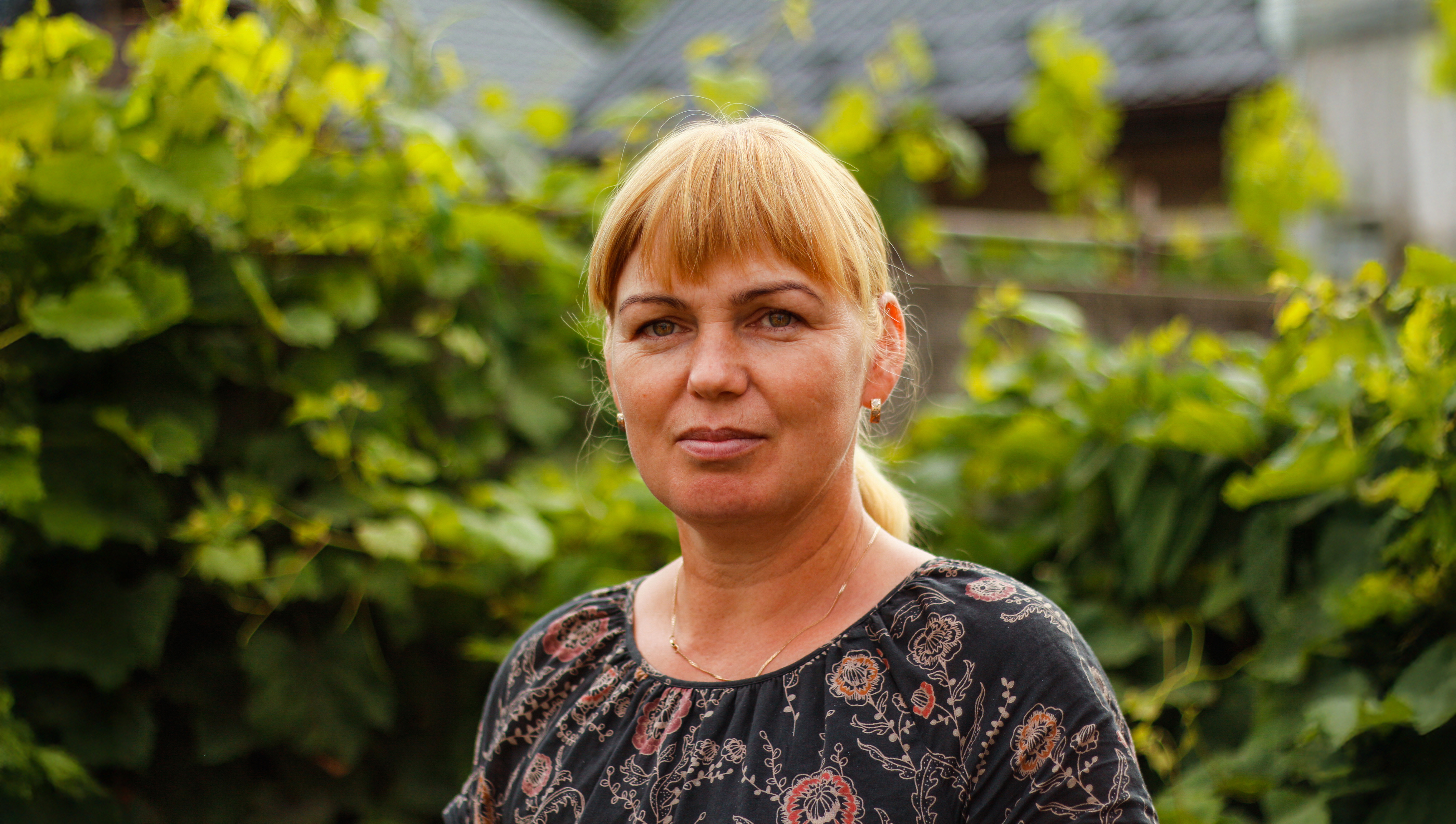 Frau mit roten Haaren, einem Pony und mit Pferdeschwanz, um die 40 in grüner Umgebung, mit ernstem Gesichtsausdruck